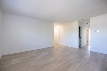 The living room and dining room of an apartment with white walls and wood floors